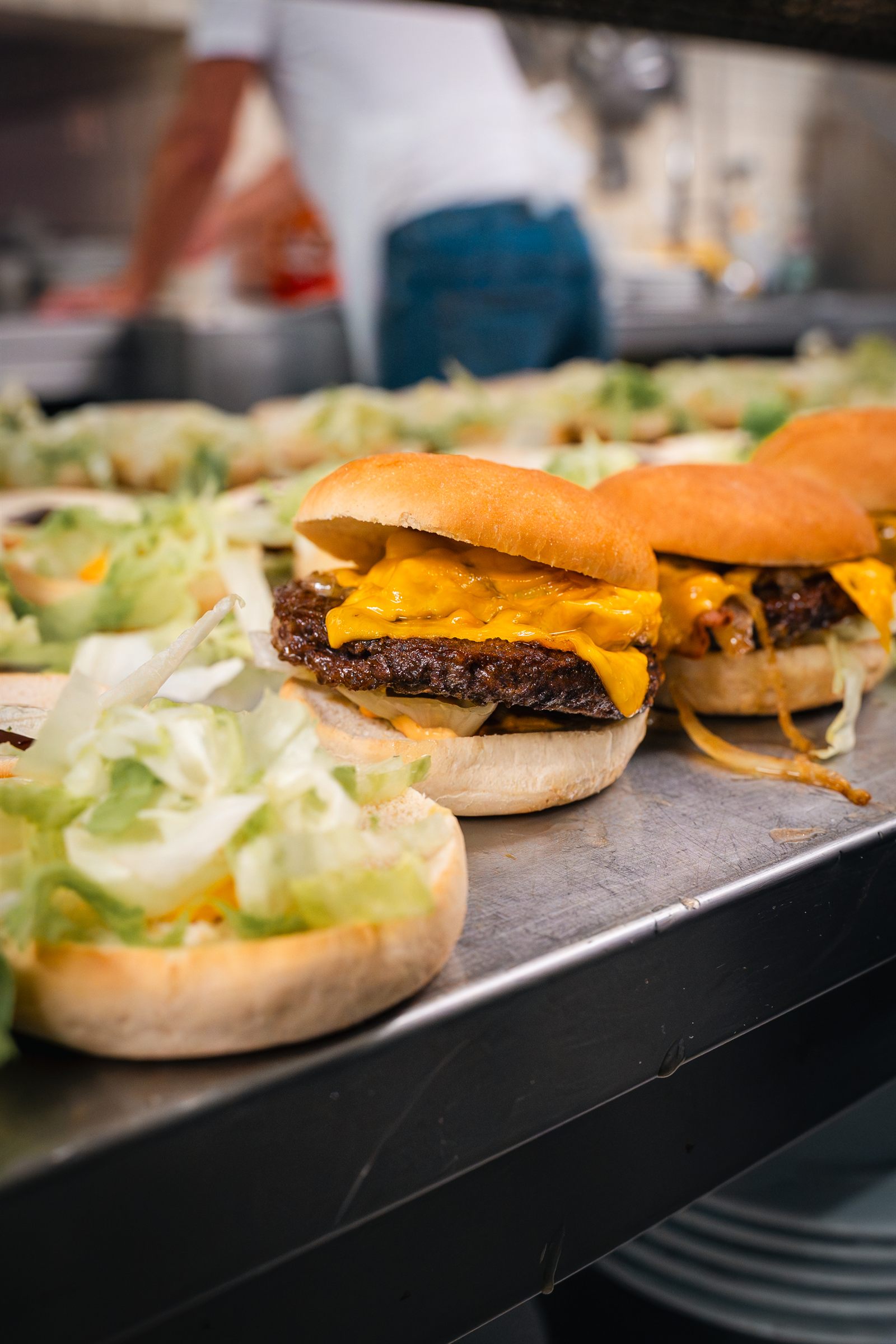 Frisch angerichtete Cheeseburger am Küchenpass, dahinter die Küche