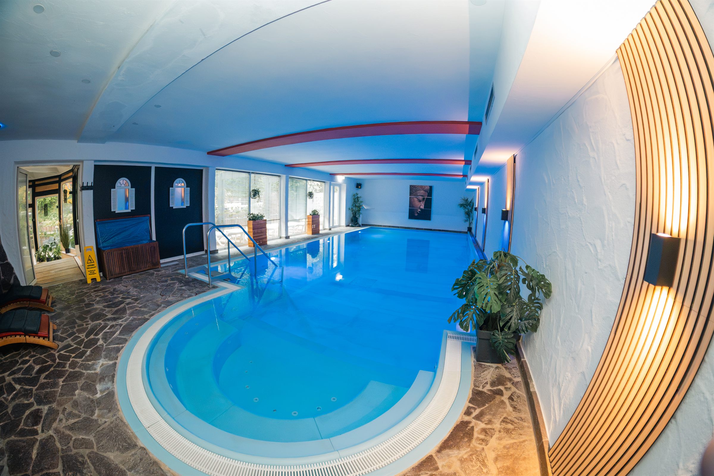 Schwimmbad mit rundem Beckenteil, Natursteinboden und warmem Wandlicht