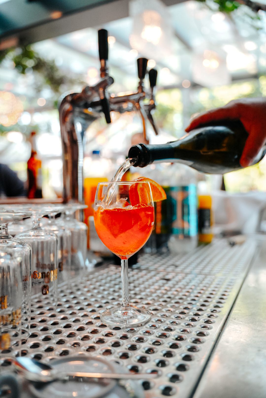 Ein Spritz wird an der Theke zubereitet: Prosecco fließt ins Glas mit Eis und Orangenscheibe